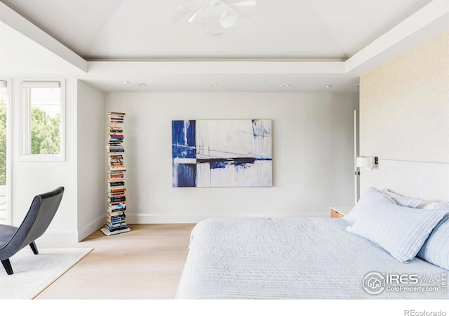 bedroom with light hardwood / wood-style floors and a raised ceiling