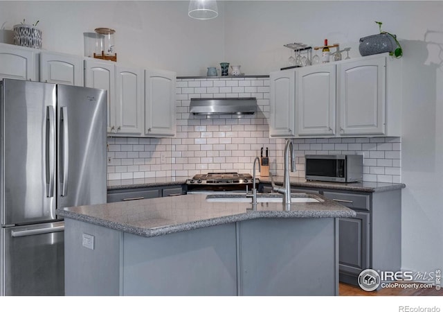 kitchen featuring sink, a kitchen island with sink, stainless steel appliances, range hood, and decorative backsplash