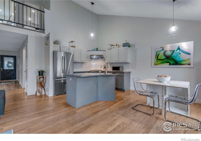 kitchen with gray cabinetry, backsplash, exhaust hood, a kitchen island with sink, and appliances with stainless steel finishes