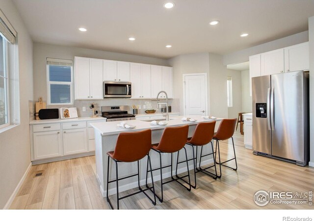 kitchen with a center island with sink, stainless steel appliances, light wood-type flooring, white cabinets, and sink