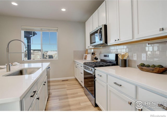 kitchen featuring decorative backsplash, sink, light hardwood / wood-style flooring, appliances with stainless steel finishes, and white cabinets