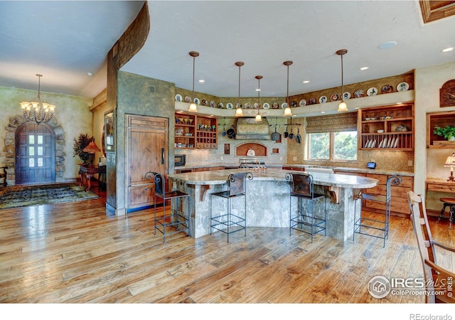 kitchen featuring pendant lighting, a kitchen bar, an inviting chandelier, light hardwood / wood-style floors, and light stone counters