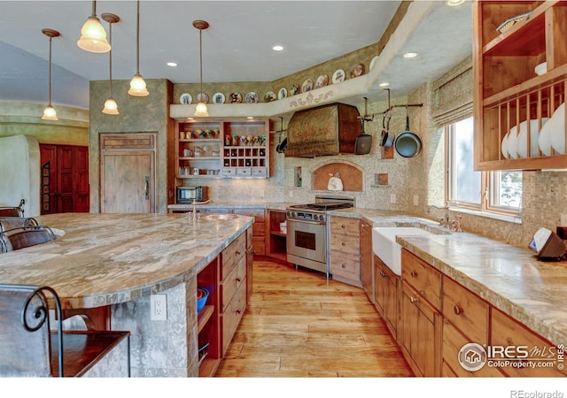 kitchen featuring premium range hood, a kitchen island with sink, hanging light fixtures, sink, and high end stainless steel range oven