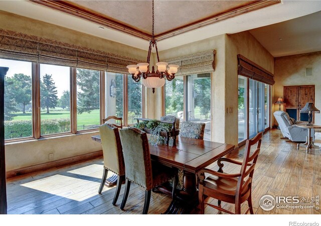 dining space featuring hardwood / wood-style flooring, a notable chandelier, a raised ceiling, and ornamental molding