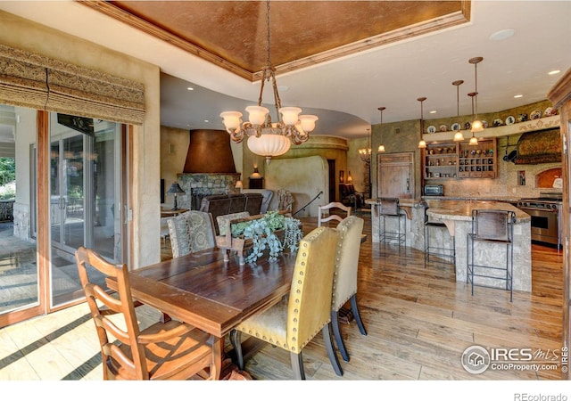 dining room with an inviting chandelier, crown molding, indoor bar, a tray ceiling, and light wood-type flooring