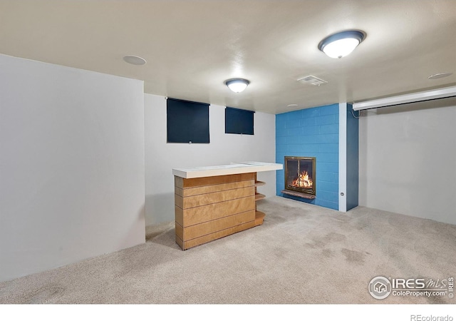 basement featuring light colored carpet and a large fireplace