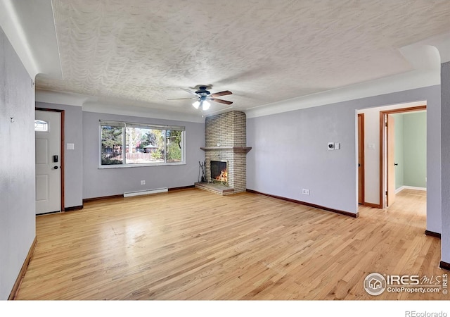 unfurnished living room with ceiling fan, a baseboard heating unit, a textured ceiling, a brick fireplace, and light wood-type flooring