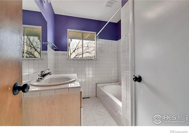 bathroom featuring tiled shower / bath, vanity, tile patterned flooring, and tile walls