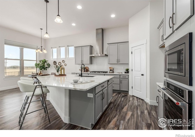 kitchen with appliances with stainless steel finishes, gray cabinetry, sink, wall chimney range hood, and decorative light fixtures