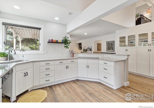 kitchen with white cabinets, sink, stainless steel dishwasher, light wood-type flooring, and kitchen peninsula