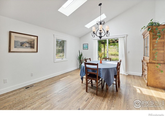 dining area with lofted ceiling with skylight, light hardwood / wood-style flooring, and a chandelier