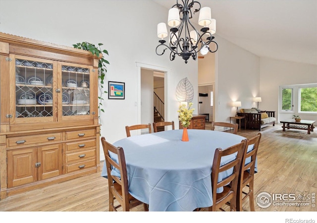 dining room with light hardwood / wood-style floors, high vaulted ceiling, and a notable chandelier