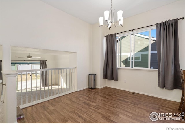 empty room with a healthy amount of sunlight, wood-type flooring, and ceiling fan with notable chandelier