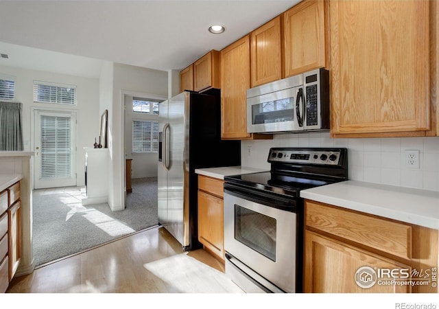 kitchen with appliances with stainless steel finishes, light wood-type flooring, and backsplash