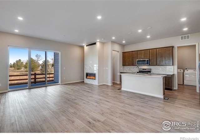 kitchen with stainless steel appliances, independent washer and dryer, a kitchen island with sink, a fireplace, and light wood-type flooring