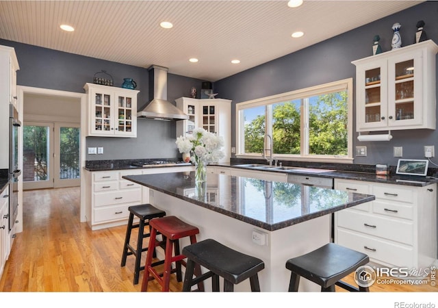 kitchen with white cabinets, a kitchen breakfast bar, sink, and wall chimney range hood