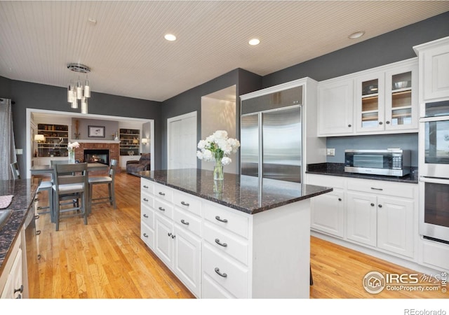 kitchen featuring a fireplace, stainless steel appliances, decorative light fixtures, light hardwood / wood-style flooring, and white cabinets