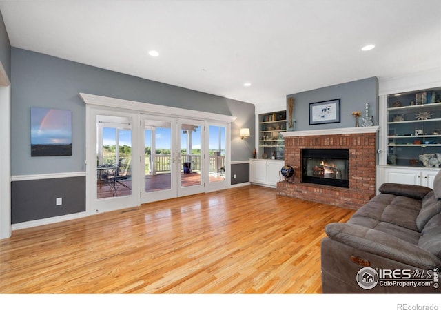 living room with built in shelves, a fireplace, wood-type flooring, and french doors