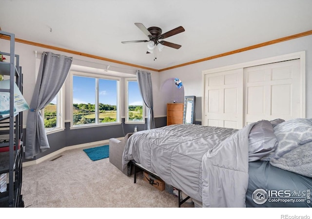 carpeted bedroom with ceiling fan, ornamental molding, and a closet