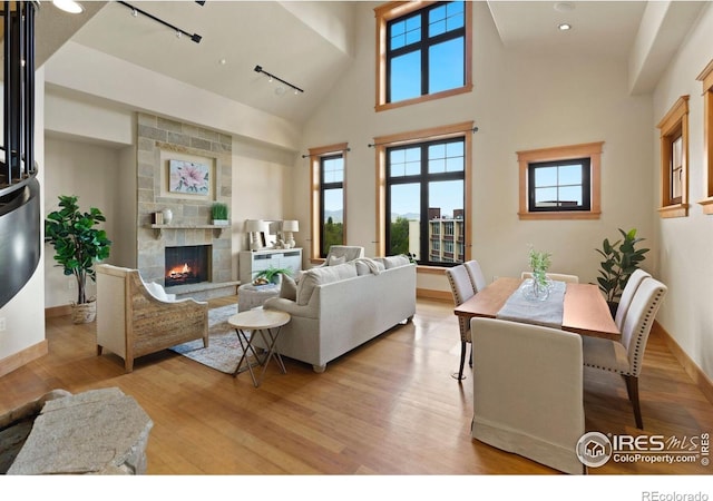 living room with a large fireplace, light wood-type flooring, a high ceiling, and track lighting