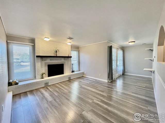 unfurnished living room featuring wood-type flooring, a brick fireplace, and a wealth of natural light