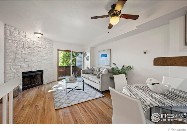 living room with hardwood / wood-style flooring, ceiling fan, and a stone fireplace