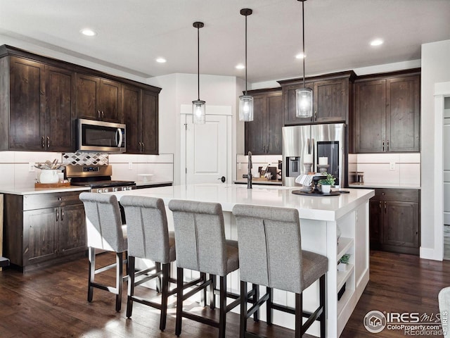 kitchen featuring a center island with sink, hanging light fixtures, dark hardwood / wood-style flooring, dark brown cabinetry, and stainless steel appliances