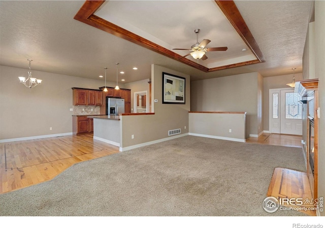 unfurnished living room featuring light carpet, ceiling fan with notable chandelier, and a tray ceiling