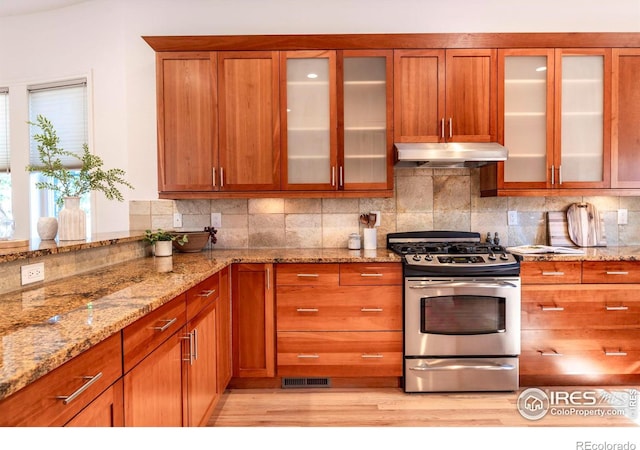 kitchen featuring decorative backsplash, light stone counters, light hardwood / wood-style flooring, and stainless steel gas range