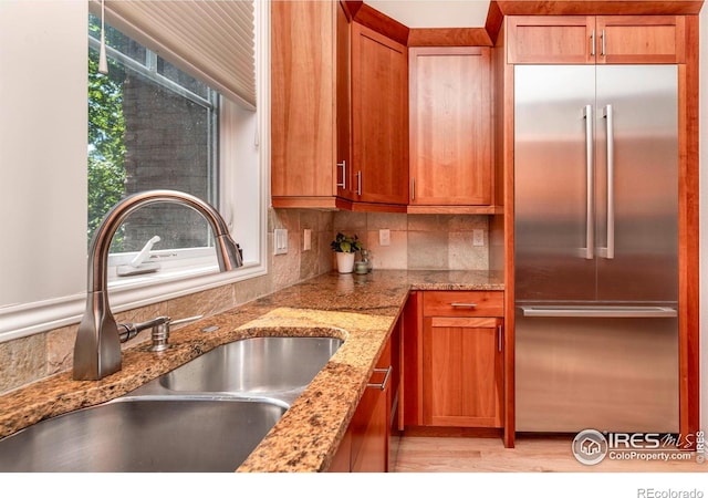 kitchen featuring backsplash, light stone countertops, sink, and stainless steel built in refrigerator