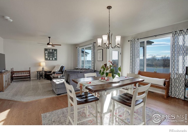 dining room with ceiling fan with notable chandelier, a water view, light hardwood / wood-style flooring, and a healthy amount of sunlight