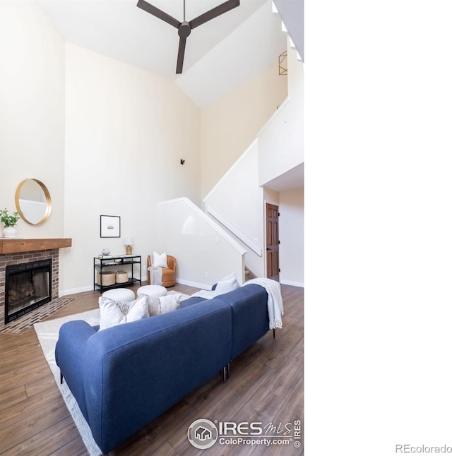 living room featuring a fireplace, high vaulted ceiling, baseboards, and wood finished floors