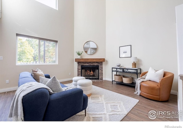 living room featuring a towering ceiling, a brick fireplace, baseboards, and wood finished floors