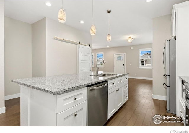 kitchen with appliances with stainless steel finishes, a kitchen island with sink, sink, a barn door, and white cabinets