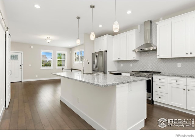 kitchen featuring white cabinetry, a kitchen island with sink, wall chimney range hood, and appliances with stainless steel finishes