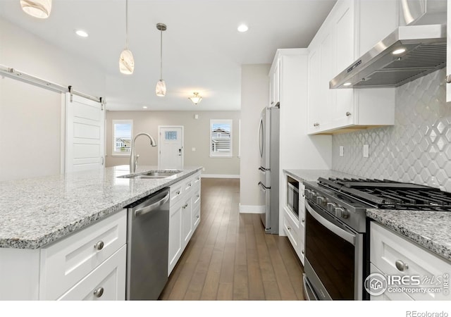 kitchen with appliances with stainless steel finishes, wall chimney exhaust hood, sink, a barn door, and white cabinetry