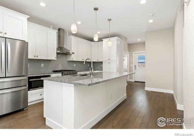 kitchen featuring light stone countertops, sink, wall chimney range hood, a center island with sink, and stainless steel refrigerator