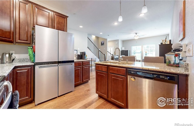 kitchen featuring sink, decorative light fixtures, stainless steel appliances, light stone countertops, and light hardwood / wood-style floors