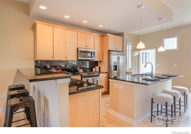 kitchen featuring dark countertops, appliances with stainless steel finishes, a kitchen breakfast bar, light brown cabinets, and a sink