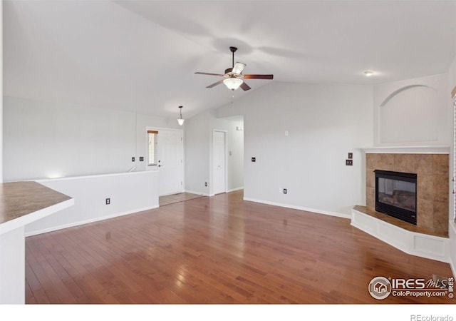 unfurnished living room with a tile fireplace, dark hardwood / wood-style floors, vaulted ceiling, and ceiling fan