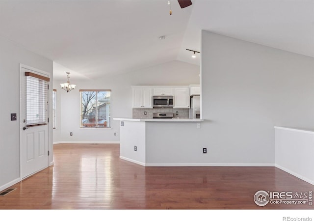 kitchen featuring white cabinetry, backsplash, kitchen peninsula, vaulted ceiling, and appliances with stainless steel finishes