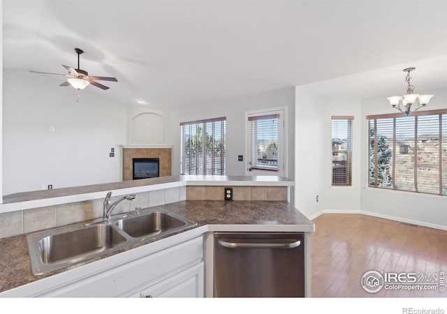 kitchen featuring a tile fireplace, white cabinets, sink, hanging light fixtures, and stainless steel dishwasher