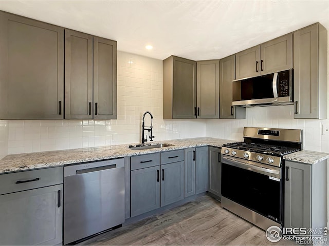 kitchen featuring gray cabinetry, sink, appliances with stainless steel finishes, light hardwood / wood-style floors, and light stone counters