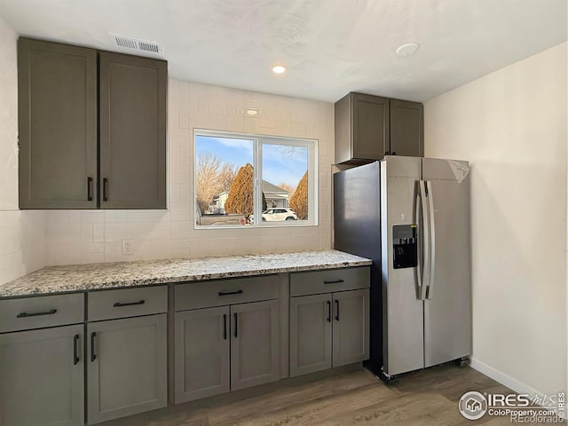 kitchen featuring decorative backsplash, gray cabinets, stainless steel fridge, light stone countertops, and wood-type flooring