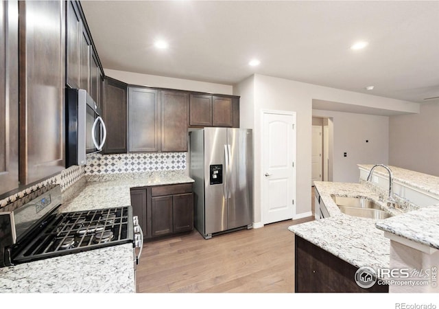 kitchen with dark brown cabinetry, sink, stainless steel appliances, light stone counters, and backsplash