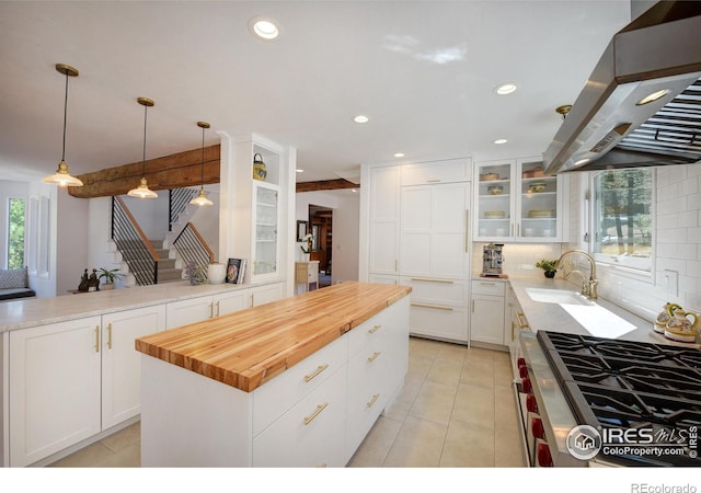 kitchen featuring island range hood, white cabinets, glass insert cabinets, hanging light fixtures, and a sink