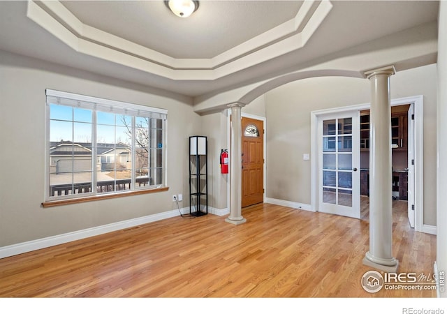 entrance foyer with decorative columns, a raised ceiling, and light wood-type flooring