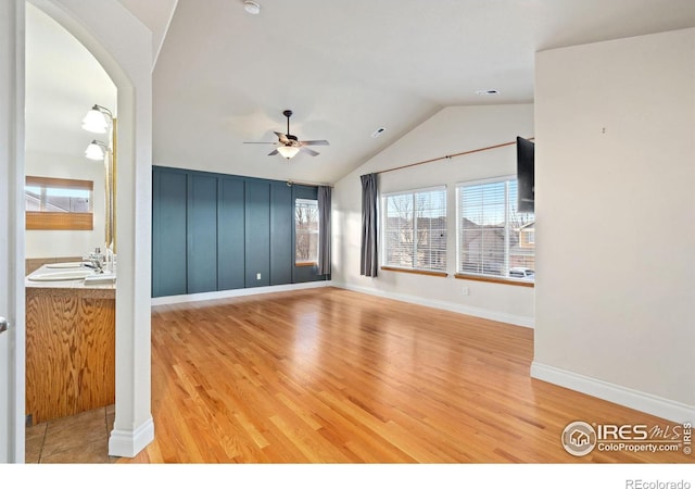 unfurnished living room with ceiling fan, vaulted ceiling, sink, and wood-type flooring