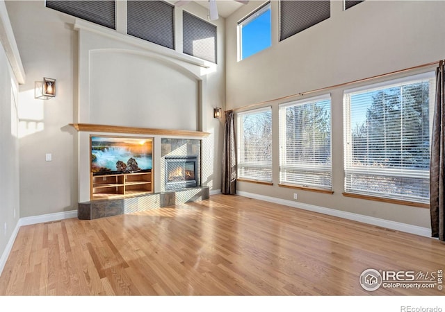 unfurnished living room featuring a tiled fireplace, a towering ceiling, and light wood-type flooring