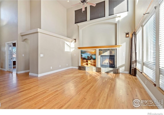 unfurnished living room featuring hardwood / wood-style flooring, a towering ceiling, a healthy amount of sunlight, and a tile fireplace